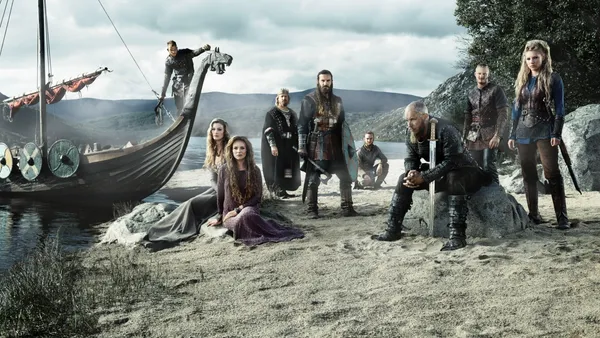 Group of Vikings stand on a beach with their boat