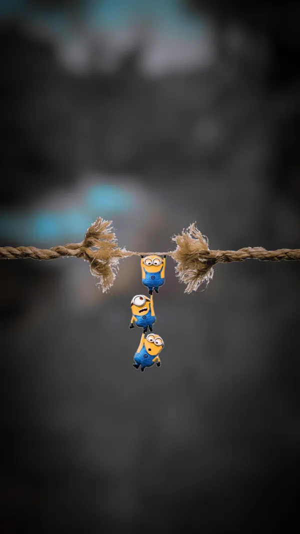 Three minions hanging from a fraying rope over a dark background